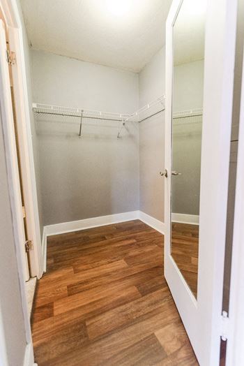 A walk in closet with a mirror and a wood floor
